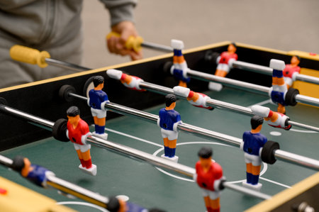 Close-up of a foosball table featuring vibrant player figures in blue and red, with a hand gripping...