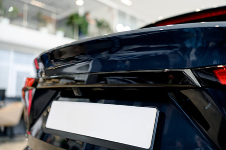 Close-up of the rear of a modern car featuring a blank license plate, displayed in a bright dealership showroom with plants in the background