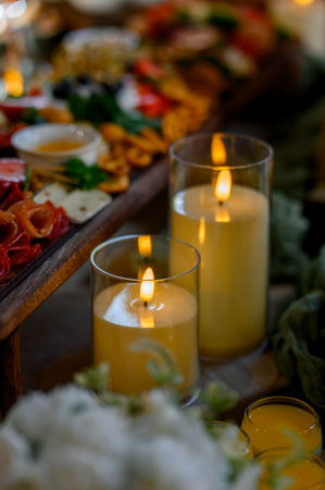 Three glass candles illuminate a beautifully arranged platter of gourmet food on a wooden table,...