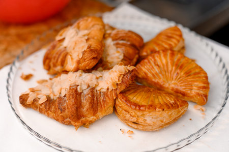 A variety of pastries including flaky croissants and sweet baked goods arranged on a glass plate,...