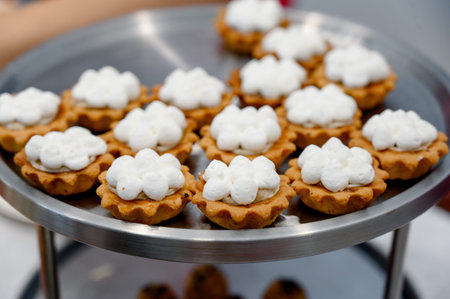 A variety of small dessert tarts topped with fluffy whipped cream arranged neatly on a round metal...