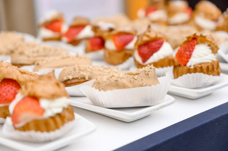 A variety of pastries filled with cream and topped with strawberries are arranged on small plates at...