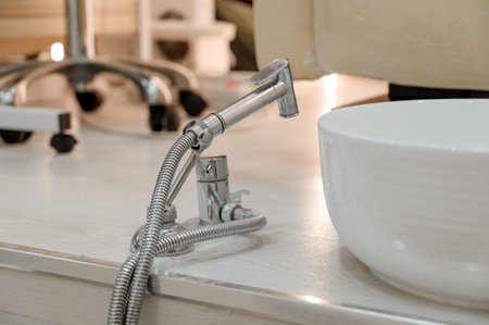 Close-up of a modern bathroom faucet with a flexible hose connected to a white ceramic sink on a...