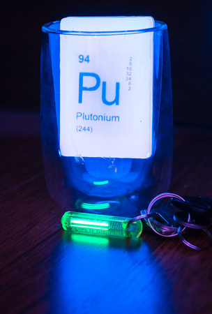 Green glowing tritium trinket on wooden desktop with luminescent soapの写真素材