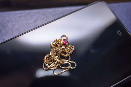 A closeup view of a ruby ??stone with gold necklace on black cell phone surfaceの写真素材
