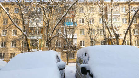 Snow covered Moscow yard with sunny residential house wall and naked tree branches in winterの写真素材