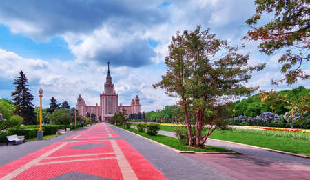 Campus of famous university with blossoming trees, benches and red bike road under dramatic cloudy sky in spring Moscowのeditorial素材