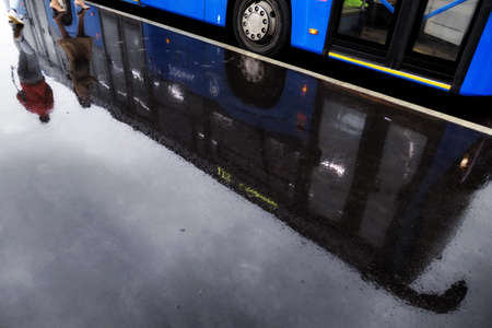 Water reflections of Moscow street in wet rainy asphalt road with ladies and blue busの写真素材
