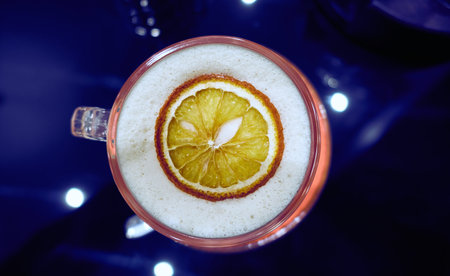 Hot coffee mug with slice of dried lime on white foam with dark blue reflecting backgroundの写真素材