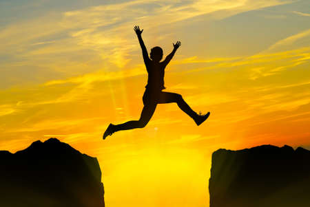 Silhouette of young person jumping over the mountains at sunset
