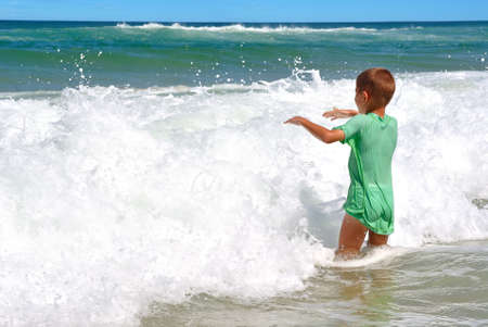 Happy boy having fun in the waves on tropical beachの写真素材