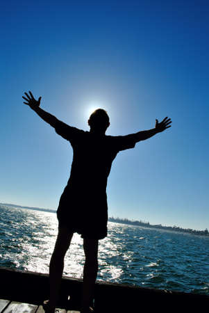 Silhouette of a man standing on a pier facing sun with open arms