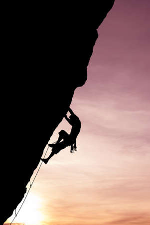 Silhouette of a climber on a vertical wall over beautiful sunsetの写真素材