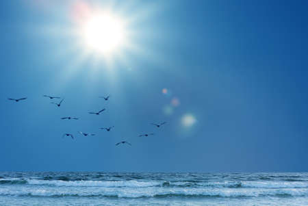 Sun shining in blue sky over ocean wavesの写真素材