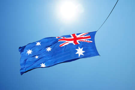 Australian flag blows in the wind against blue sky backgroundの写真素材