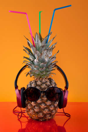 Pineapple with straws, glasses, and headphones on a colored backgroundの写真素材