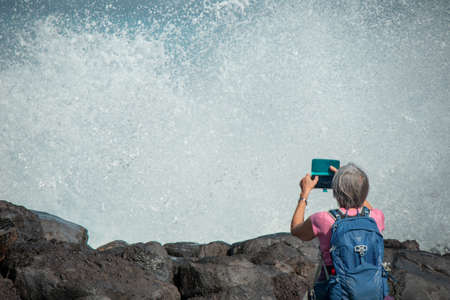 A tourist shoots big waves on the ocean shoreの写真素材