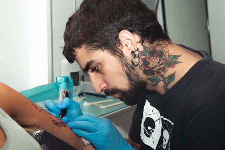 A tattoo artist paints a client's tattoo with ink. Tattoo artist holding a tattoo machine in Blue...