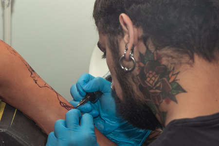 A tattoo artist paints a client's tattoo with ink. Tattoo artist holding a tattoo machine in Blue...