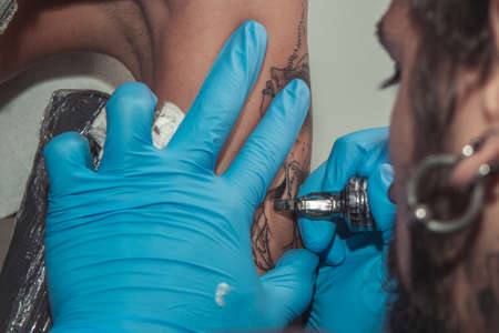 A tattoo artist paints a client's tattoo with ink. Tattoo artist holding a tattoo machine in Blue...