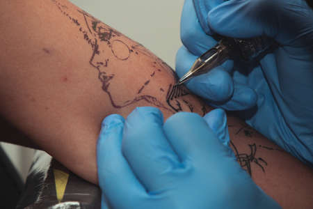 A tattoo artist paints a client's tattoo with ink. Tattoo artist holding a tattoo machine in Blue...
