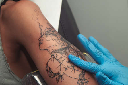 A tattoo artist paints a client's tattoo with ink. Tattoo artist holding a tattoo machine in Blue...