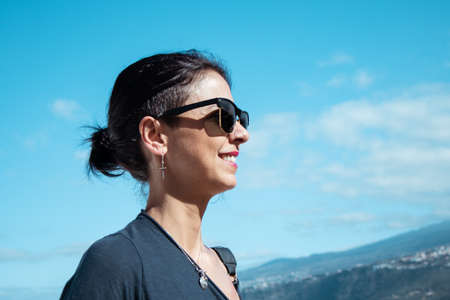 A woman with sunglasses smiles against the blue skyの写真素材