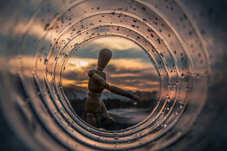 Wooden dummy at sunset of the ocean, shot through a transparent tube with drops of waterの写真素材