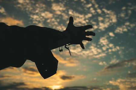 Silhouette of a hand against a sky background with clouds at sunsetの写真素材