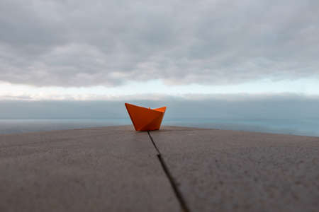 Paper orange boat on a railing with sky and ocean backgroundの写真素材