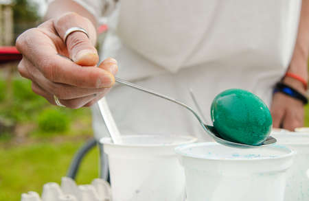 The hand holds a spoon and pulls out a green egg from Easter paints