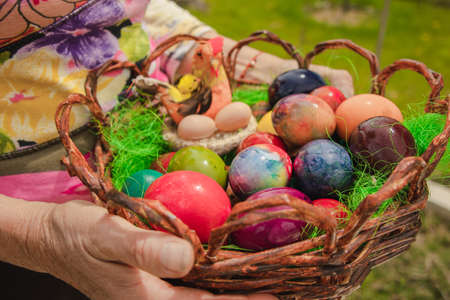 An elderly woman's hands holding a basket of colorful Easter eggs