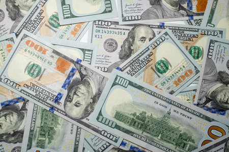 An array of hundred dollar bills is arranged closely together, showing the intricate designs and...