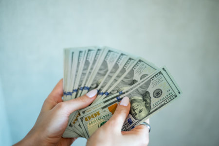 Counting cash in hands with hundred dollar bills in a modern indoor setting under natural lightの写真素材