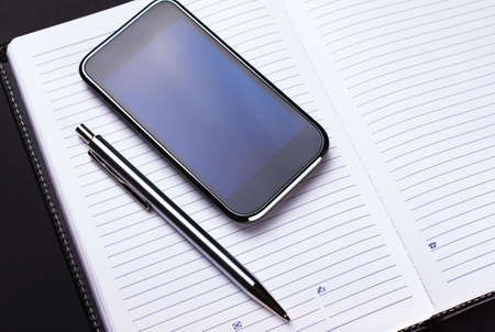 phone, pen and notebook on blackの写真素材