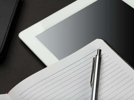 Workplace with blank digital tablet, notebook and pen on black background