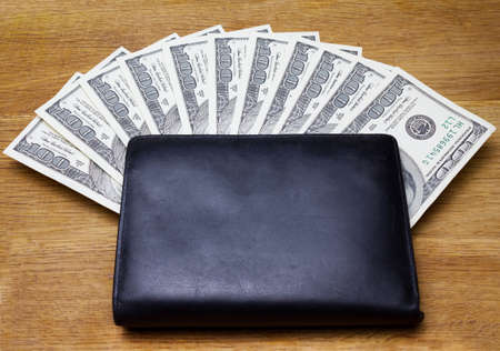 black leather wallet with money on wooden background