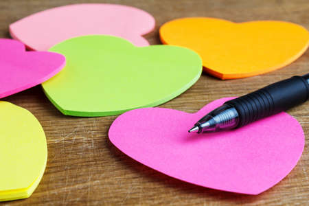 Sheets of paper in the shape of a heart with pen on a wooden table