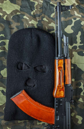 Ski mask and ak 47 on a camouflage background, close up