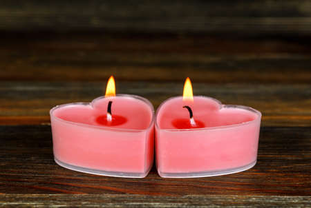Two burning candles in the shape of a heart on wood close-upの写真素材
