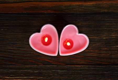 Two burning candles in the shape of a heart on wood close-upの写真素材