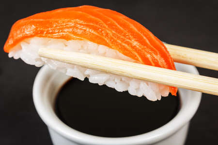 Close-up of sushi with chopsticks and soy sauce on black backgroundの写真素材