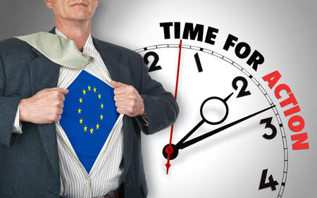Businessman showing superhero suit with flag from Europe underneath his shirt standing against clock...