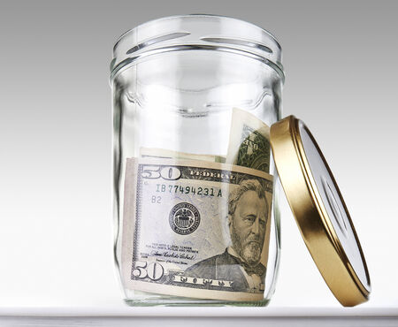 US dollars bank notes in a glass opened jar on a grey gradient background