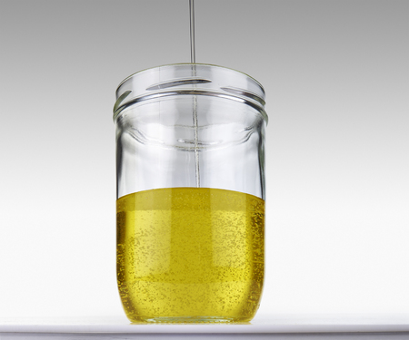 Olive oil flowing into glass jar on a grey gradient backgroundの写真素材