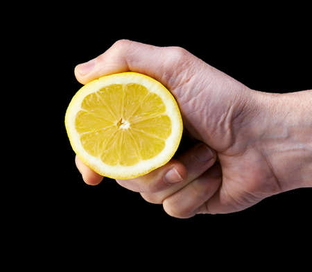 Man's hand squeezing half of lemon on black background