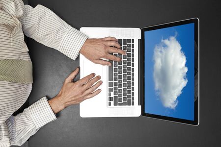 Businessman wearing a white shirt and green tie working on his laptop. Cloud computing on screenの写真素材