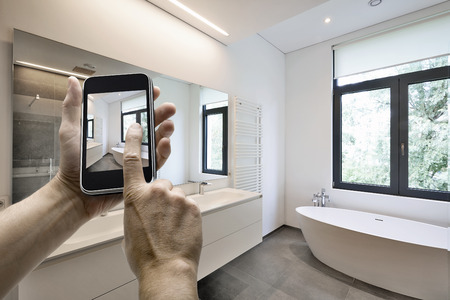 Mobile device with man hands taking picture in  tiled bathroom with windows towards garden