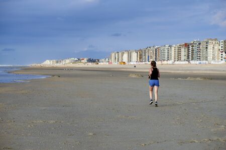 DE PANNE, BELGIUM - JULY 03, 2017: Woman jogging on the beach of the Belgian Seaside resort De Panne early in the morningのeditorial素材