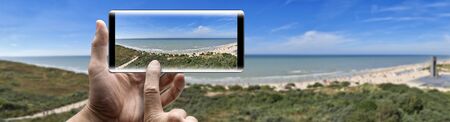 Two hands holding a mobile Smartphone and take a picture of Summer beach panorama sceneの写真素材